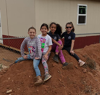 Four students sitting on a dirt pile.